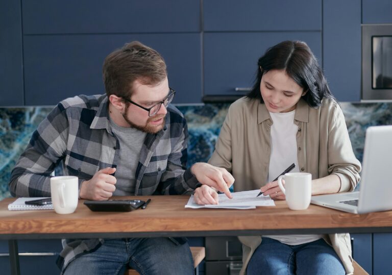 Two spouses sitting at a table as one signs legal documents, representing how property and home ownership are reviewed during divorce proceedings